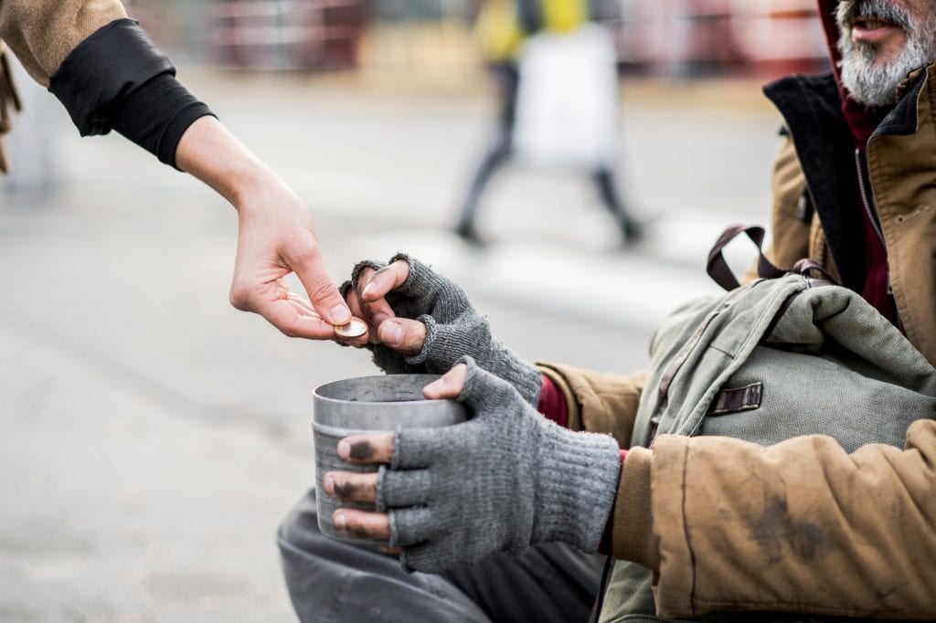 A midsection of woman giving money to homeless beggar man sitting in city.